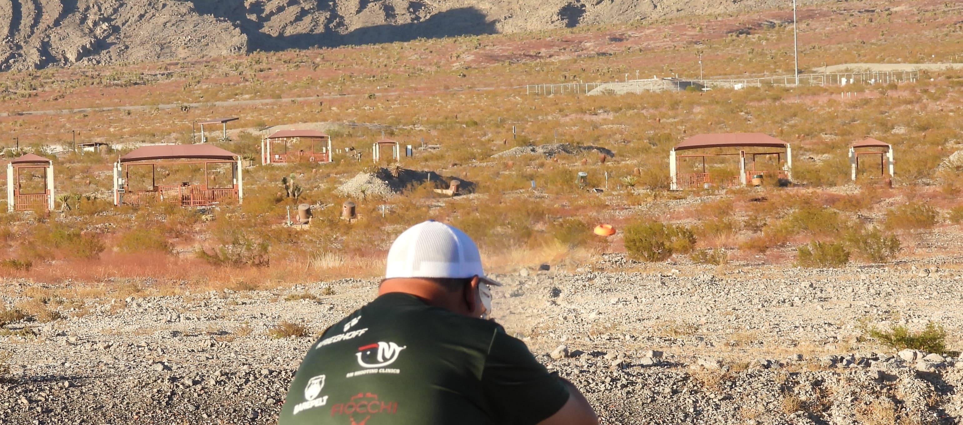 Shooter aiming downrange with trap houses and desert mountains